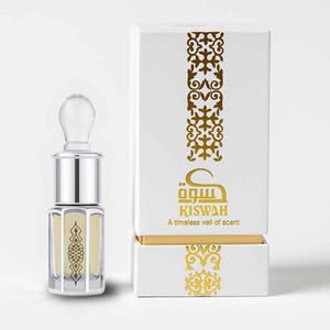 Può includere: Un flacone di profumo con un tappo in vetro trasparente e una base in metallo argentato, accanto a una scatola bianca. Il flacone e la scatola presentano motivi decorativi dorati e il testo "KISWAH: A timeless veil of scent."