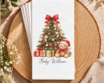 Può includere: Una pila di tovaglioli di carta bianchi con un'illustrazione stampata di un albero di Natale decorato con un grande fiocco rosso in cima, regali alla base e un orsacchiotto con un cappello da Babbo Natale. Il testo Baby William è stampato sotto.