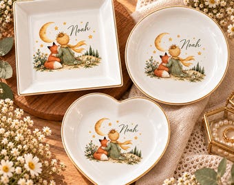 Può includere: Tre piattini in ceramica bianca con bordi dorati, di forma quadrata, rotonda e a cuore. Ogni piattino presenta un'illustrazione di un piccolo principe e una volpe seduti sotto una luna crescente con il nome Noah scritto in corsivo.
