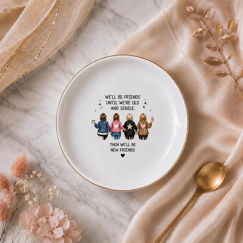 Puede incluir: Un plato decorativo redondo de cer&aacute;mica blanca con un borde dorado. El centro presenta una ilustraci&oacute;n de cuatro amigos de pie uno al lado del otro con el texto: WE'LL BE FRIENDS UNTIL WE'RE OLD AND SENILE. THEN WE'LL BE NEW FRIENDS.