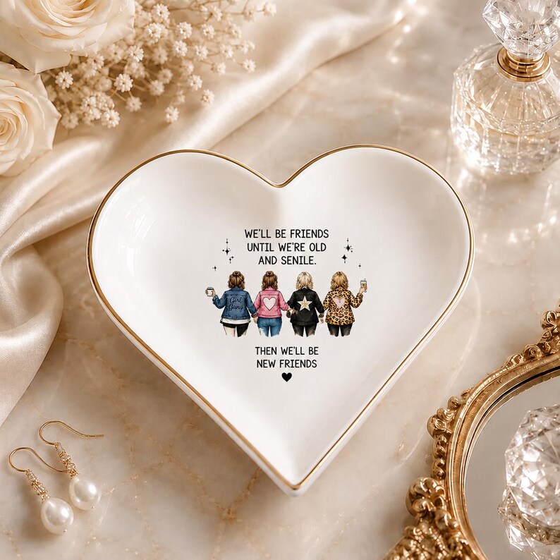 Puede incluir: Un plato de cer&aacute;mica blanco en forma de coraz&oacute;n con un borde dorado. El centro presenta una ilustraci&oacute;n de cuatro amigos vistos desde atr&aacute;s y el texto: WE'LL BE FRIENDS UNTIL WE'RE OLD AND SENILE. THEN WE'LL BE NEW FRIENDS con un peque&ntilde;o coraz&oacute;n negro.