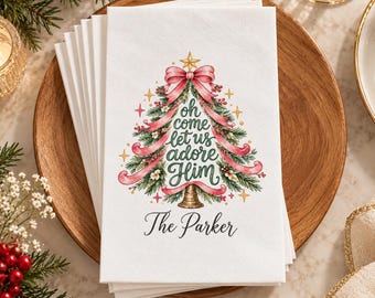Può includere: Una pila di tovaglioli di carta bianca con un'illustrazione stampata di un albero di Natale verde decorato con un nastro rosa, una stella dorata e bacche rosse. Il testo recita "oh come let us adore Him" e "The Parker" in corsivo nero.