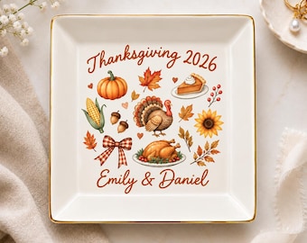 Può includere: Un piattino quadrato in ceramica bianca con bordo dorato e una grafica Thanksgiving 2026. Il design include un tacchino, zucca, mais, torta, girasole, ghiande e un fiocco a quadri, con il testo Emily & Daniel stampato in arancione.