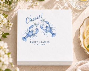 Può includere: Un tovagliolo di carta quadrato bianco con un'illustrazione ad acquerello blu di due aragoste che tengono dei bicchieri da martini. Il testo Cheers! è stampato in blu sopra, con i nomi EMILY + JAMES e la data 07.01.2026 sotto.