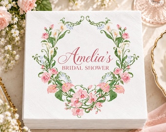 Può includere: Un tovagliolo di carta quadrato bianco con un'illustrazione di ghirlanda floreale nei toni del rosa, verde e bianco. Il centro della ghirlanda contiene il testo Amelia's BRIDAL SHOWER in un carattere rosa corsivo e serif, circondato da rose e gigli.