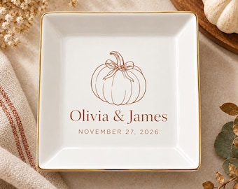 Può includere: Un piattino quadrato in ceramica bianca con bordo dorato. Al centro presenta un'illustrazione a linee marroni di una zucca con un fiocco, i nomi Olivia & James e la data NOVEMBER 27, 2026, stampati con un carattere serif marrone.