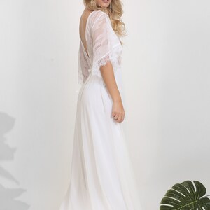 May include: A white lace wedding dress with a flowing skirt and a low back. The dress has a delicate lace overlay and a simple, elegant design.
