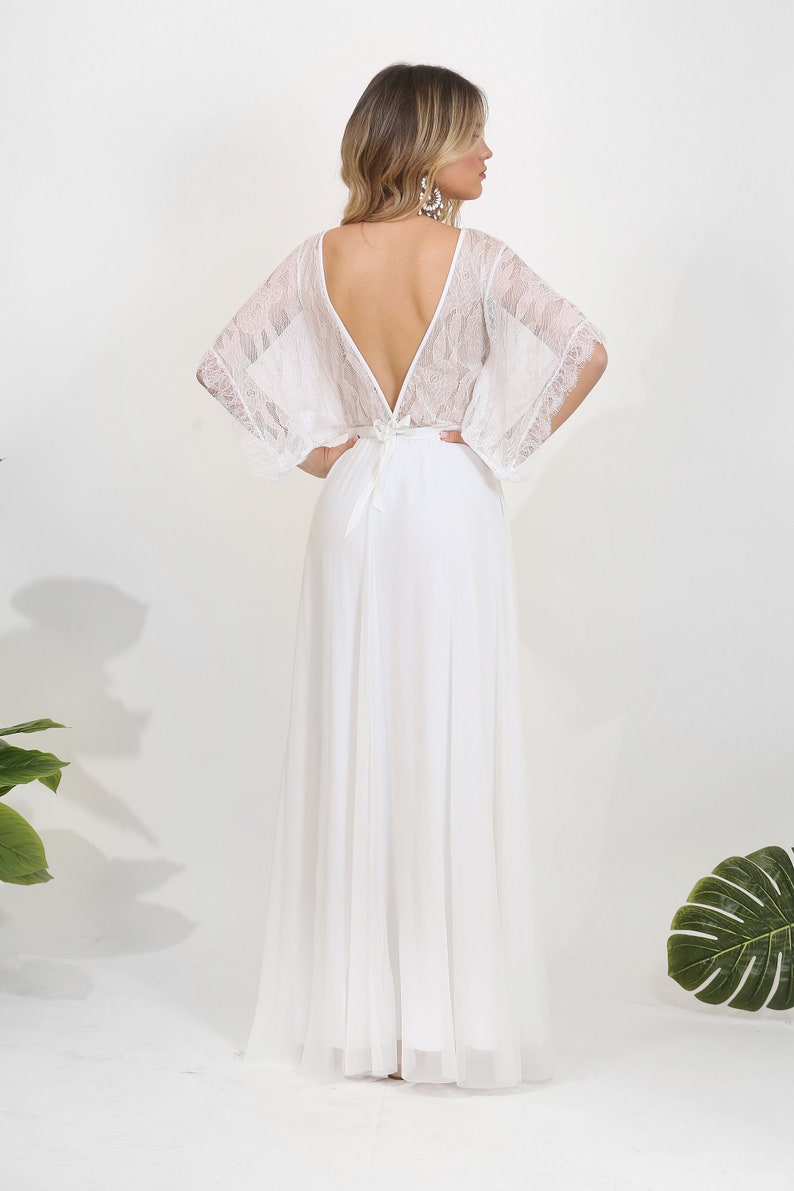 May include: A white maxi dress with a lace bodice and long sleeves. The dress has a deep V-neckline and a tie at the back.