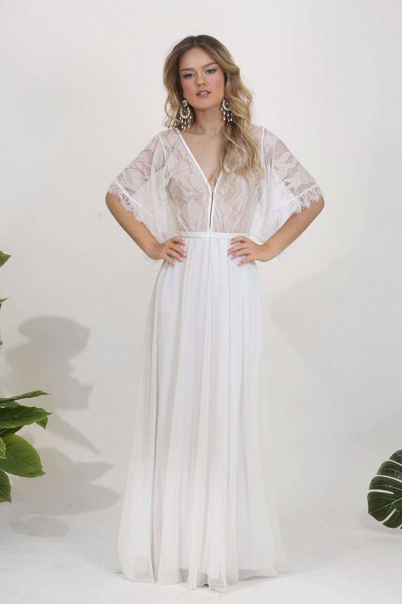 May include: A white lace and chiffon maxi dress with a V-neckline and a fitted bodice. The dress has a flowy skirt and short, bell sleeves with lace trim.