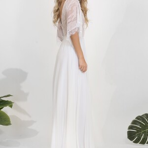 May include: A white lace and chiffon wedding dress with a flowing skirt and a lace overlay on the bodice. The dress has a deep V-neckline and short sleeves.