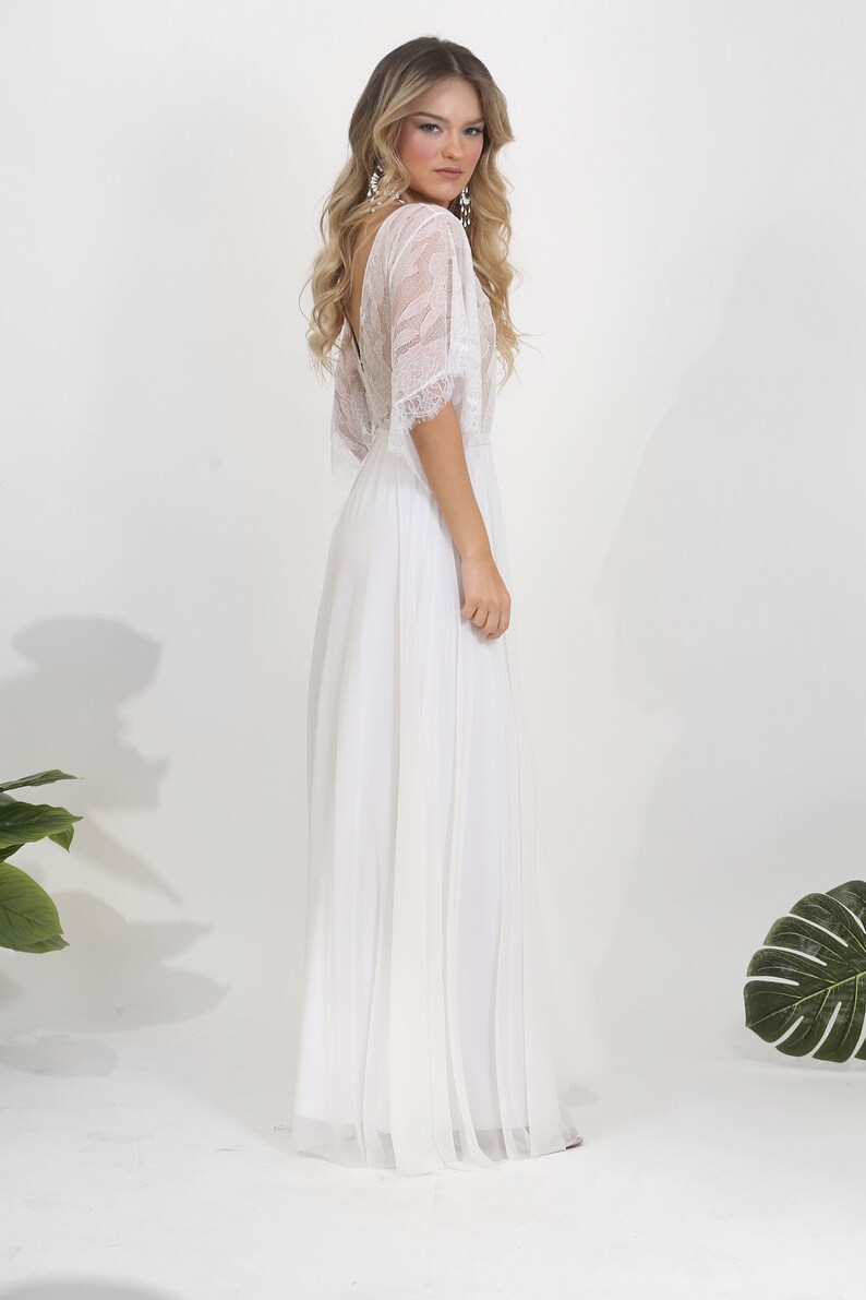 May include: A white lace and chiffon wedding dress with a flowing skirt and a lace overlay on the bodice. The dress has a deep V-neckline and short sleeves.
