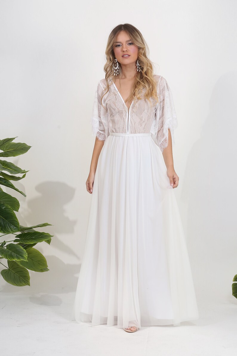 May include: A white lace wedding dress with a V-neckline and a flowing skirt. The dress has a sheer overlay and a delicate lace pattern.