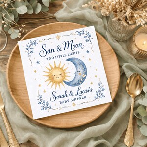 May include: A square paper napkin featuring a watercolor illustration of a smiling sun and a crescent moon. The text reads Sun & Moon TWO LITTLE LIGHTS and Sarah & Lucas's BABY SHOWER in blue script and block lettering with gold stars and blue vines.