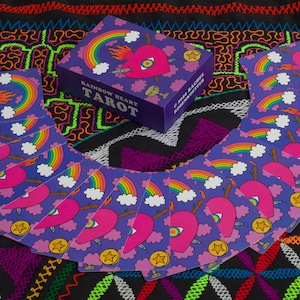 Rainbow Heart Tarot deck card box and card backs displayed on Shipibo embroidered tapestry featuring flower of life design