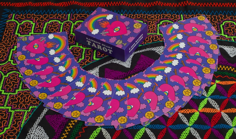 Rainbow Heart Tarot deck card box and card backs displayed on Shipibo embroidered tapestry featuring flower of life design