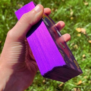 Purple metallic card edges of the Rainbow Heart Tarot deck with a green lawn in the background