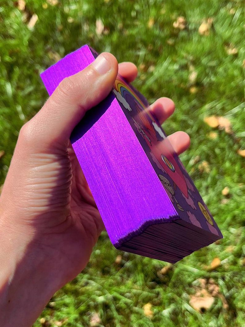 Purple metallic card edges of the Rainbow Heart Tarot deck with a green lawn in the background