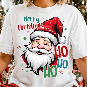 May include: White t-shirt featuring a graphic of Santa Claus wearing a red hat with white trim. The text "Merry Christmas" is above Santa, and "HO HO HO" is below. Festive stars and snowflakes surround the design.
