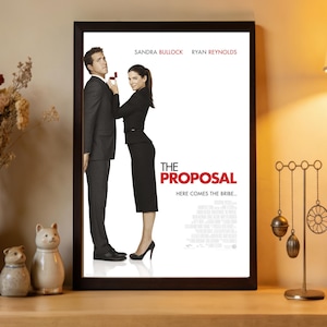 Pode incluir: Pôster emoldurado do filme "A Proposta" com Sandra Bullock e Ryan Reynolds. O pôster mostra os atores em trajes formais, com a mulher segurando uma caixa de anéis. O título e o slogan do filme são exibidos em destaque.