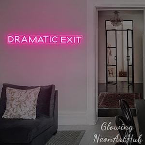 May include: A pink neon sign that reads "DRAMATIC EXIT" is mounted on a light pink wall. The sign illuminates the room, which includes a dark gray sofa with a decorative pillow and a doorway leading to another room.