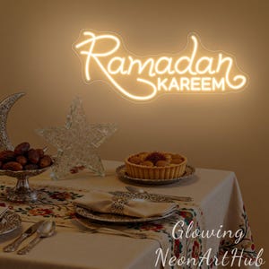 May include: A warm-toned image features a neon sign that reads "Ramadan Kareem." A table is set with a decorative tablecloth, silverware, and a tart. Other decorations include a crescent moon, a star, and a bowl of dates.