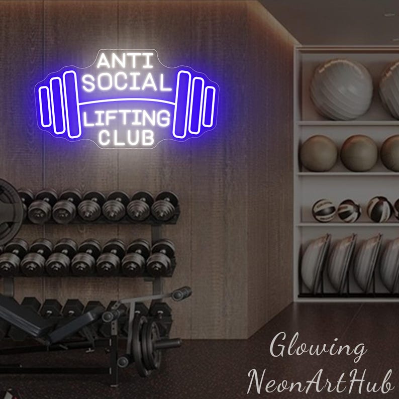 Pu&ograve; includere: Un'insegna al neon con la scritta "ANTI SOCIAL LIFTING CLUB" in bianco e blu, a forma di bilanciere. Lo sfondo mostra una palestra con manubri, dischi e palle da ginnastica.