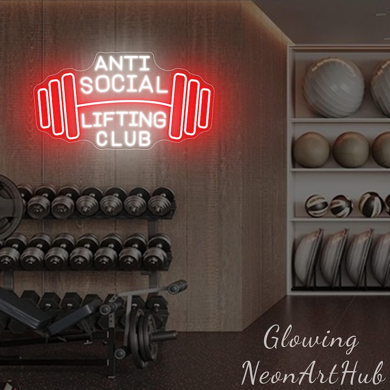Pu&ograve; includere: Un'insegna al neon rossa e bianca con la scritta "ANTI SOCIAL LIFTING CLUB" in una palestra. L'insegna ha la forma di un bilanciere. Manubri e palle da ginnastica sono visibili sullo sfondo.