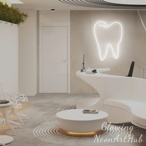 Puede incluir: Interior de una moderna clínica dental con mostrador de recepción blanco y sala de espera. Un letrero de neón con forma de diente está montado en la pared. Las palabras "Glowing NeonArtHub" son visibles en la esquina inferior derecha.