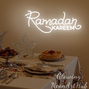 May include: A white neon sign that reads "Ramadan Kareem" is displayed above a table set for a meal. The table is set with a patterned tablecloth, silverware, and a tart. A decorative star and crescent moon are also on the table.