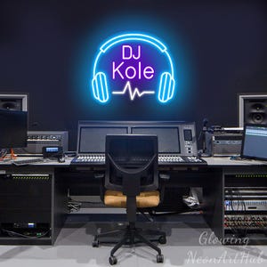Puede incluir: Un letrero de neón brillante azul y blanco montado en una pared oscura, con el texto DJ Kole en una fuente estilizada, colocado sobre unos auriculares y un gráfico de onda sonora. El letrero emite un brillo vibrante sobre el fondo oscuro.