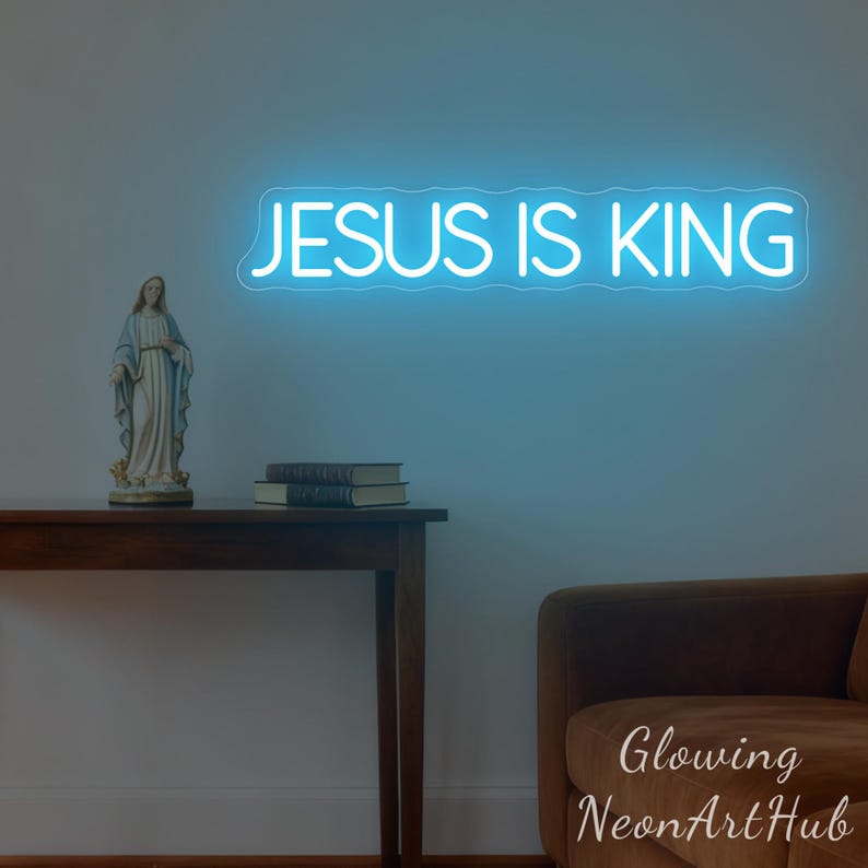 May include: A blue neon sign that reads "JESUS IS KING" is mounted on a wall. A statue of a religious figure and two books sit on a wooden table. A brown sofa is in the lower right corner.