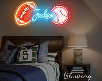 May include: A neon sign featuring a football and a baseball, connected by a blue neon line with the name "Jackson" in cursive. The football is orange with white details, and the baseball is white with red stitching. The sign is mounted on a wall above a bed.