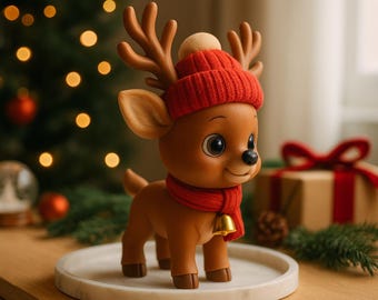 Könnte beinhalten: Eine braune Rentierfigur mit roter Strickmütze, Schal und goldener Glocke. Das Rentier hat große Augen und steht auf einem weißen, kreisförmigen Tablett. Weihnachtsdekorationen im Hintergrund, darunter ein Weihnachtsbaum und ein Geschenk.
