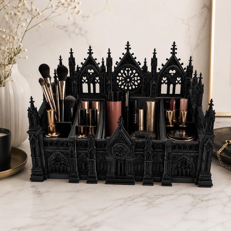 Puede incluir: Un organizador de maquillaje negro de estilo g&oacute;tico con m&uacute;ltiples compartimentos. El organizador tiene forma de catedral, con intrincados detalles arquitect&oacute;nicos. Contiene varios art&iacute;culos de maquillaje, incluyendo brochas, pintalabios y otros productos de belleza.