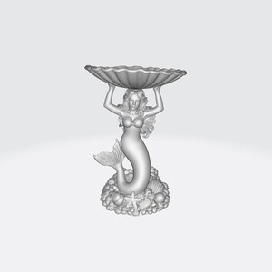 Pu&ograve; includere: Una scultura dettagliata di una sirena che tiene una grande conchiglia smerlata sopra la sua testa. La sirena ha capelli fluenti e una coda di pesce. La base presenta conchiglie, stelle marine e altri elementi marini. La scultura &egrave; di colore grigio chiaro.