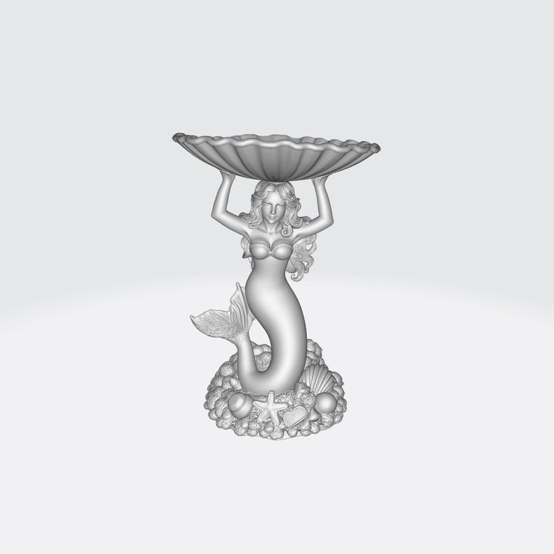 Pu&ograve; includere: Una scultura dettagliata di una sirena che tiene una grande conchiglia smerlata sopra la sua testa. La sirena ha capelli fluenti e una coda di pesce. La base presenta conchiglie, stelle marine e altri elementi marini. La scultura &egrave; di colore grigio chiaro.