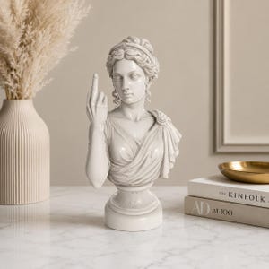 May include: A white bust of a classical figure, sculpted with intricate details, is shown giving the middle finger. The statue has a draped garment and a detailed hairstyle. The bust is on a pedestal base, and the overall aesthetic is a blend of classical art and modern humor.