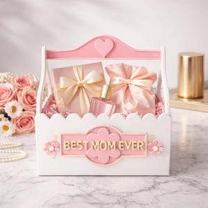 May include: A white and pink gift basket with the text "BEST MOM EVER" contains a wrapped gift, a satin pouch, and a perfume bottle. The basket is decorated with pink flowers and a heart.