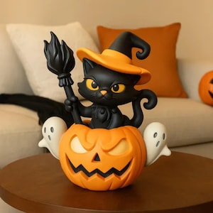 Könnte beinhalten: Eine Halloween-Figur mit einer schwarzen Katze, die einen Hexenhut trägt und einen Besen hält, der aus einem orangefarbenen Kürbis kommt. Zwei weiße Geister flankieren den Kürbis. Die Figur steht auf einem braunen Tisch.
