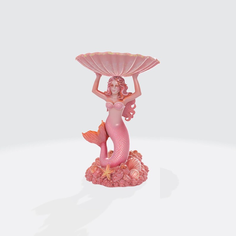 Pu&ograve; includere: Una statuetta di sirena rosa che tiene una grande conchiglia smerlata. La sirena ha i capelli rosa e una coda abbinata. La base &egrave; decorata con conchiglie e una stella marina. Un elemento decorativo.