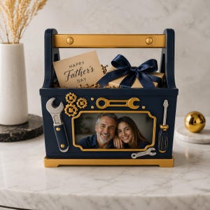 Puede incluir: Un marco de fotos en forma de caja de herramientas azul marino con detalles dorados. El marco presenta una foto de una pareja sonriente, herramientas decorativas y una tarjeta que dice "Happy Father's Day". Una caja de regalo con un lazo azul marino está dentro.