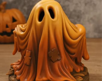 Może przedstawiać: Figurka na Halloween przedstawiająca ducha w pomarańczowo-żółtym odcieniu. Duch ma dwa owalne otwory na oczy i dwie brązowe łaty na swoim drapowanym prześcieradle. Figurka stoi na brązowej podstawie w kształcie liścia, z wyrzeźbioną dynią w tle.
