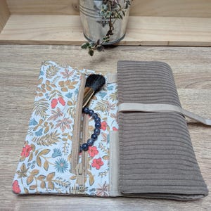 Puede incluir: Un organizador enrollable con exterior de pana marrón y forro interior blanco con un colorido estampado floral de hojas y flores rojas, azules y bronceadas. Incluye un bolsillo con cremallera que contiene una brocha y una pulsera de cuentas.