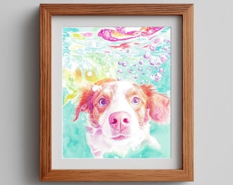 Könnte beinhalten: Aquarellmalerei eines Hundes unter Wasser, gerahmt in einem Holzrahmen. Der Hund hat weißes und braunes Fell, eine rosa Nase und Ohren und ist von Blasen und farbigem Wasser umgeben. Das Kunstwerk ist eine Nahaufnahme des Gesichts des Hundes.