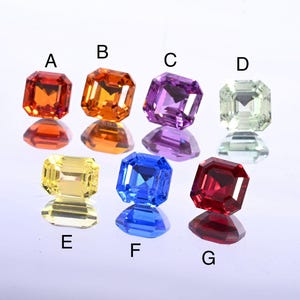 May include: Seven colorful, faceted gemstones in shades of orange, yellow, purple, green, blue, and red. Each gem has a square cut with a reflective surface, creating a sparkling effect. The gems are labeled A through G.