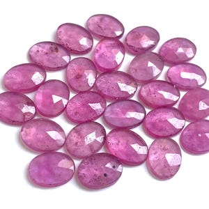 Puede incluir: Un conjunto de gemas facetadas de forma ovalada en tonos rosa y magenta. Las gemas están dispersas sobre una superficie blanca, mostrando sus facetas pulidas y su claridad interna. Ideales para la creación de joyas.