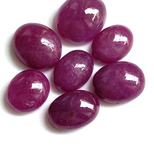 Puede incluir: Colección de siete piedras preciosas ovaladas pulidas de varios tamaños. Las piedras son de un color magenta intenso y rico con una superficie brillante y reflectante. Están dispuestas sobre un fondo blanco, resaltando su color y forma.