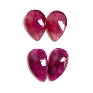 Op de afbeelding: Vier gefacetteerde, peervormige robijn edelstenen. De robijnen hebben een diepe, rijke rode kleur met kleurschakeringen en enkele insluitsels. De edelstenen zijn in paren gerangschikt op een witte achtergrond.
