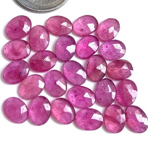 Könnte beinhalten: Eine Sammlung oval geschliffener, facettierter rosa Edelsteine. Die Edelsteine haben einen leuchtenden Rosaton mit vielen Facetten, die das Licht einfangen. Die Edelsteine sind auf einer weißen Oberfläche angeordnet.