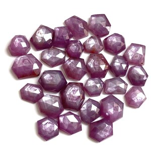Peut inclure: Une collection de pierres précieuses rouge-violettes à facettes, de formes géométriques variées. Les pierres sont disposées sur une surface blanche, mettant en valeur leurs multiples facettes et leur clarté interne. La couleur varie du rouge clair au rouge foncé.